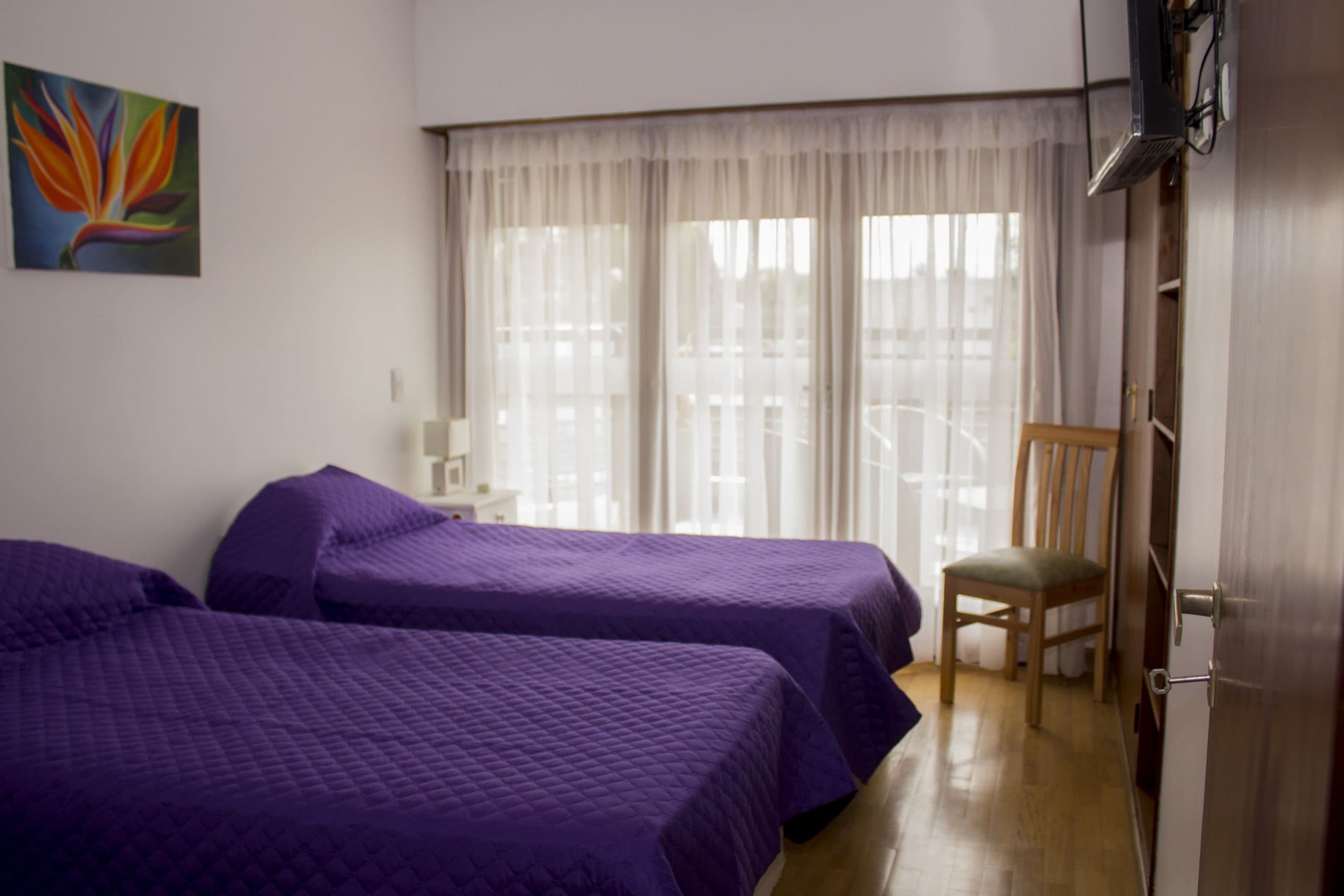 Habitación con dos camas y cubrecamas violeta, con balcón